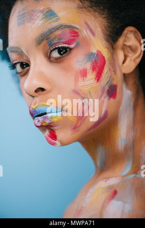 Belle jeune femme avec des traits de peinture sur visage isolé sur blue Banque D'Images