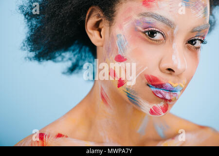 Jolie jeune femme avec des traits de couleur sur le visage à la caméra à l'isolé sur blue Banque D'Images