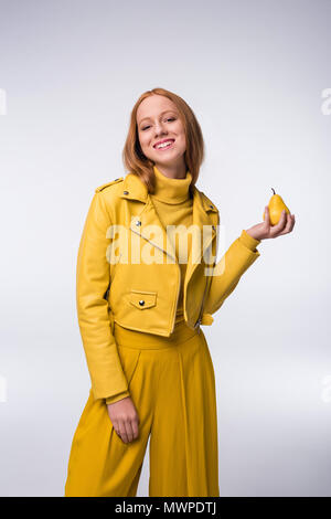 Belle fille à la mode en jaune clothes holding poire, isolé sur gray Banque D'Images