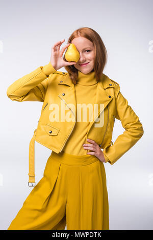 Belle rousse en fille élégante veste en cuir jaune holding poire, isolé sur gray Banque D'Images