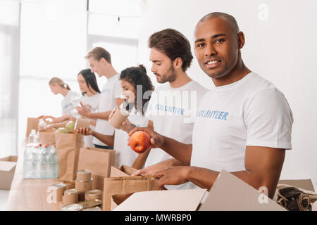African American volunteer conserve des aliments dans des sacs avec muriethnic groupe de collègues Banque D'Images