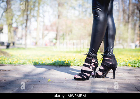 Voir les jambes d'une femme marchant avec des fleurs. La fille en pantalon noir se déplace autour de l'extérieur du parc. Concept de mode et Beuty. Banque D'Images