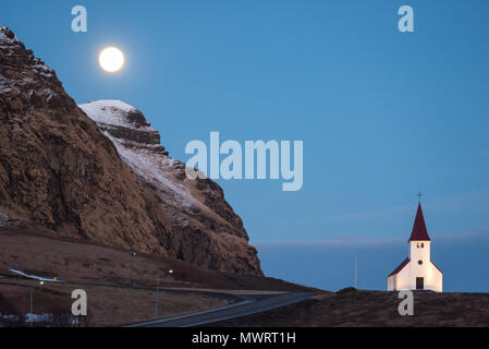 Pleine lune sur l'église de la Vik en Islande et une montagne avec une mince couche de neige Banque D'Images