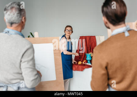 Vue arrière d'hommes artistes looking at woman holding art outils pour still life in art studio Banque D'Images