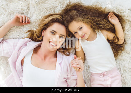 Vue de dessus d'heureuse maman et sa fille couchée sur couverture en peau de mouton et looking at camera Banque D'Images