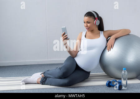 African American Woman listening music avec des écouteurs et smartphone alors qu'il était assis avec haltères et fit ball Banque D'Images