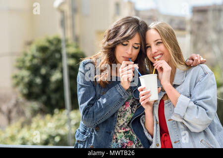 Deux jeunes femmes de boire la même emporter avec deux pailles en verre à l'extérieur. Banque D'Images