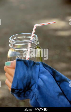 Paille en plastique et verre pot dans les mains d'un adolescent, à l'extérieur, avec de l'herbe background Banque D'Images