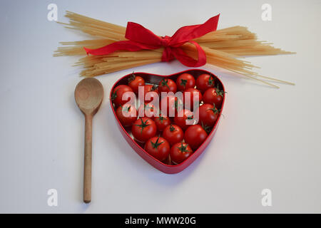 Cuillère en bois, boîte en forme de coeur de tomates fraîches et un tas de spaghettis non cuits attaché avec un ruban rouge Banque D'Images