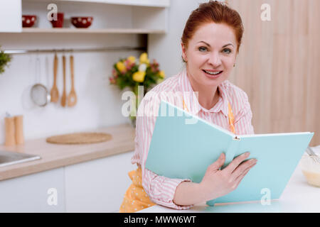 Mature femme en tablier avec livre de recettes Banque D'Images
