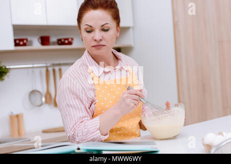 Belle femme mature pour mixer la pâte feuilletée et livre de lecture Banque D'Images