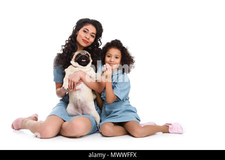 Happy mother and daughter sitting on floor with pug isolated on white Banque D'Images