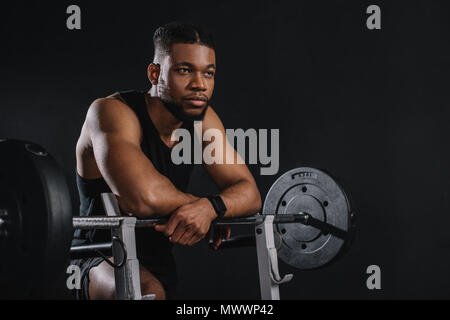 Muscular young african american sportsman à Pise et à la suite d'haltères sur noir Banque D'Images