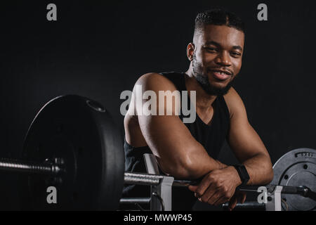 Muscular young african american sportsman à Pise et barbell smiling at camera sur noir Banque D'Images