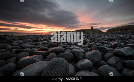 L'aube la lumière se reflétant sur les rochers au château de Dunstanburgh sur la côte nord-est, Northumberland, Angleterre, Royaume-Uni, Europe Banque D'Images