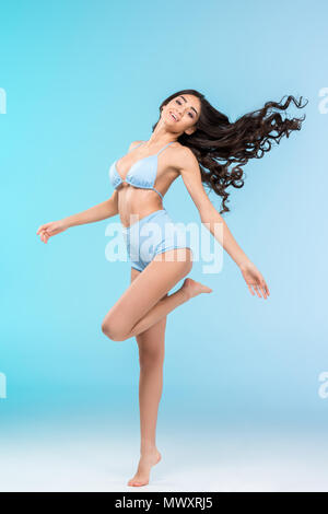 Beautiful happy brunette girl posing in bikini, isolé sur bleu Banque D'Images