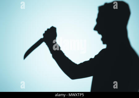 Ombre de personne en criant et en tenant le couteau sur bleu Banque D'Images