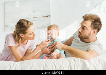 Les jeunes parents essayant de calmer les pleurs de bébé Bébé fille avec dummy Banque D'Images