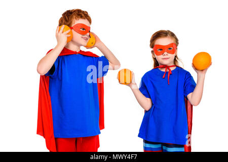 Super mignon enfants dans des masques et des capes holding oranges isolated on white Banque D'Images