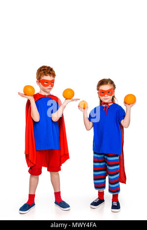 Adorables petits kids in superhero costumes holding oranges isolated on white Banque D'Images