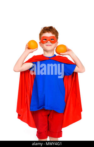 Heureux l'enfant en costume de super-héro holding oranges and smiling at camera isolated on white Banque D'Images