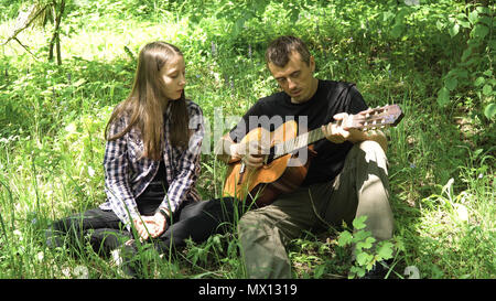 Fille aime son père pour jouer une guitare acoustique jardin. Père et sa jeune fille se jouant de la guitare dans un parc verdoyant. Banque D'Images