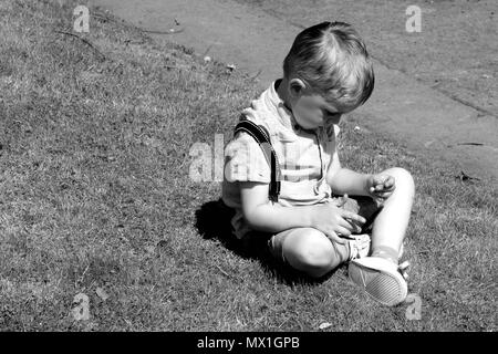 Jeune garçon dans pensée profonde assis sur l'herbe photographie noir et blanc Banque D'Images