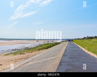 Sur le côté de l'estuaire, sur le haut d'un talus bordé de pierre des gens marcher le long d'un chemin vers la mer. Banque D'Images