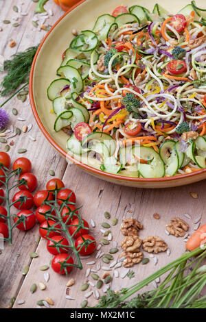 Salade de légumes renforts spiralés dans une cuvette entourée de légumes sur bois Banque D'Images