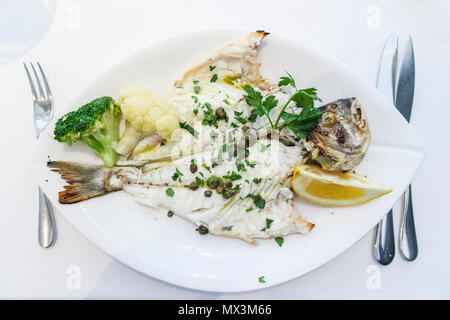 Restauration : un plat principal de la daurade dorade grillée () servi sur une plaque blanche avec une garniture de câpres, le brocoli et le chou-fleur et tranche de citron Banque D'Images