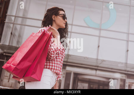 Satisfait et smiling girl holding shopping bags dans les mains. La femme montre les achats effectués, les couleurs, les tons vintage. Banque D'Images