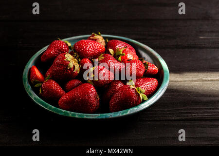 Photo : Contraste des fraises dans une assiette verte sur un tableau noir Banque D'Images