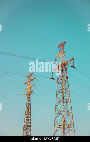 Deux grands haute tension rectangulaire tours de transmission électriques avec les lignes électriques et les arbres au-dessus des isolateurs sous ciel partiellement nuageux Banque D'Images