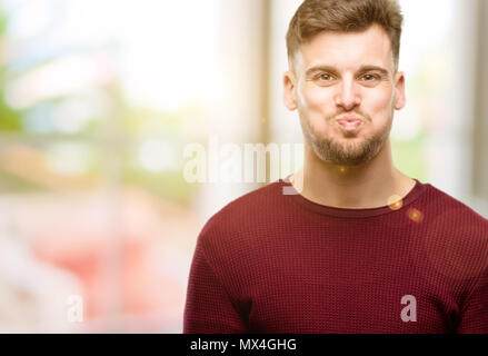 Beau jeune homme soufflant des joues, s'amusant making funny face Banque D'Images