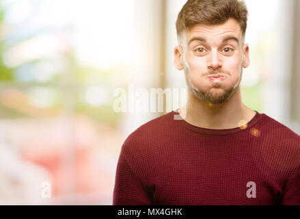 Beau jeune homme soufflant des joues, s'amusant making funny face Banque D'Images