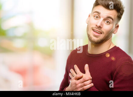 Beau jeune homme ayant charmant sourire tenant la main sur le coeur, qui souhaite montrer l'amour et de sympathie Banque D'Images