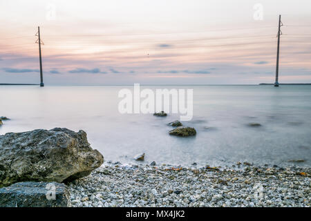 Coucher du soleil à Islamorada, Florida Keys, avec pink sky, des roches, les lignes électriques, plage de rochers, d'une exposition longue vert transparent lisse de l'eau peu profonde sur le golfe de moi Banque D'Images