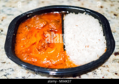 Orange red curry sauce tikka masala, gros plan macro avec riz basmati blanc en plastique noir plat fast food dîner repas congelés contenant sur le tableau Banque D'Images