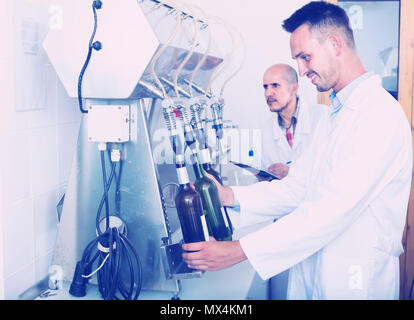 Smiling man wearing White Coat à l'aide d'équipement d'embouteillage sur la manufacture de fabrication du vin Banque D'Images