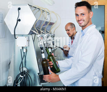 Portrait of smiling winery masculins positifs avec des travailleurs en usine sur des machines d'embouteillage Banque D'Images