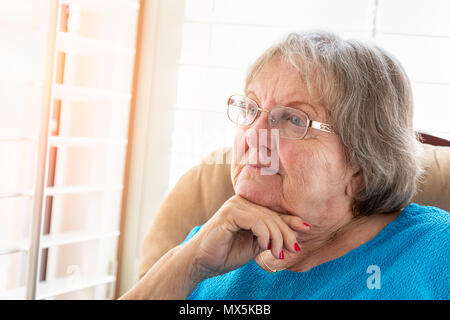 Senior Woman Gazing contemplative hors de sa fenêtre. Banque D'Images