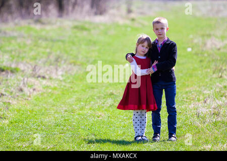 Portrait de beaux enfants dans de nouveaux habits Standing together outdoors sur fond flou lumineux, grand frère protecteur embrassant sœur. Ha Banque D'Images