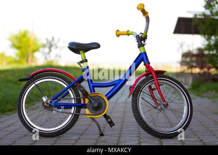 Close-up of enfant multicolore lumineux bleu, jaune et rouge sur le côté gauche de vélo appuyé en position milieu du vide pavée sur boke lumineuse floue Banque D'Images