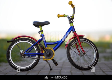 Close-up of enfant multicolore lumineux bleu, jaune et rouge sur le côté gauche de vélo appuyé en position milieu du vide pavée sur boke lumineuse floue Banque D'Images