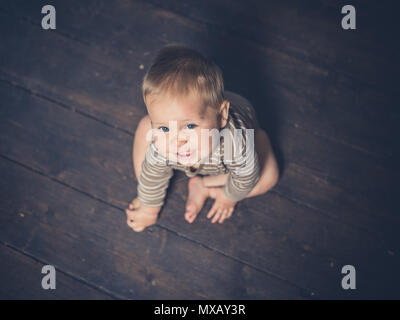 Un petit bébé est assis sur le plancher jusqu'à Banque D'Images