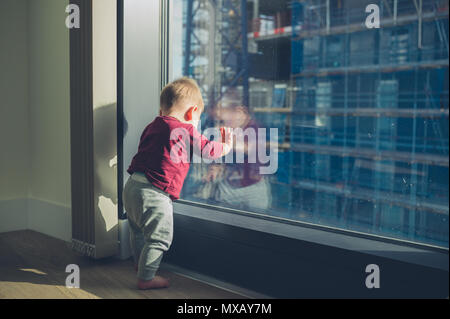 Un petit bébé est debout près de la fenêtre d'une tour d'appartement Banque D'Images