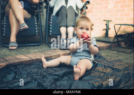Un mignon petit bébé est assis sur le sol dans le jardin et est en train de manger une pêche Banque D'Images