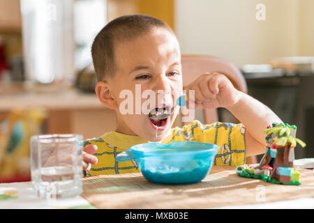 Le garçon 4 ans mange du porridge. Table enfant. Le concept de l'indépendance de l'enfant. Le garçon est déjeunant avec un appétit sur l'arrière cuisine Banque D'Images