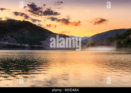 Golden sky et spectaculaire sur les nuages moelleux, soyeux réfléchissants lake et nuage de poussière volant au-dessus de l'eau de la route Banque D'Images