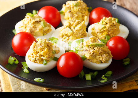 Oeufs farcis au thon en conserve et d'avocat avec tomates et oignons verts close-up sur une plaque sur une table horizontale. Banque D'Images